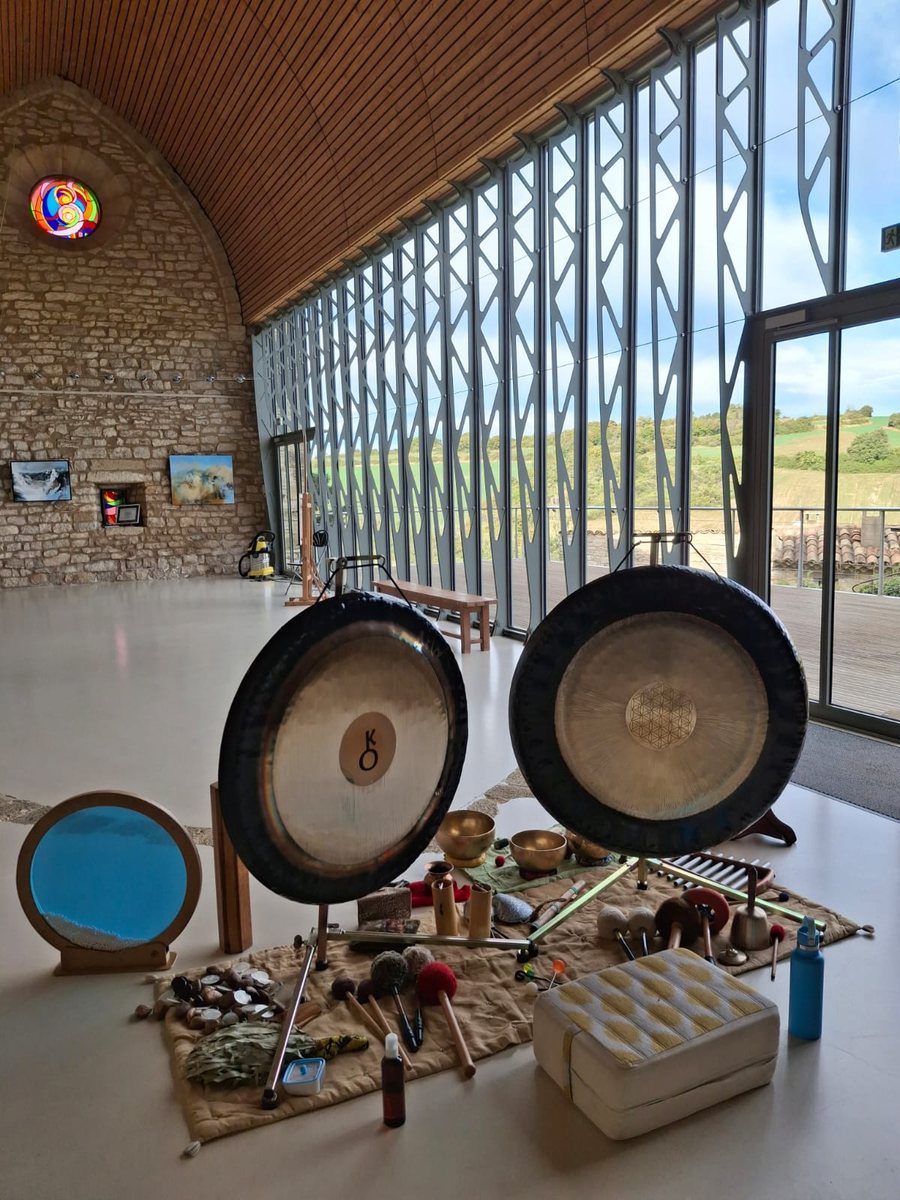 Deux gongs et des bols posés sur un tapis, dans une grande salle de pierre ouverte sur les collines